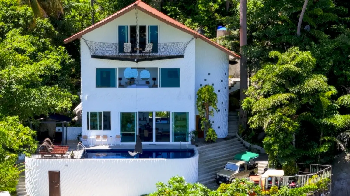 The Gardenia Luxury Villa Koh Tao, a 3-story home with 5 bedrooms and 3 bathrooms accommodating 10 guests. The design integrates natural granite boulders and tropical plants, featuring a private pool and sea views.